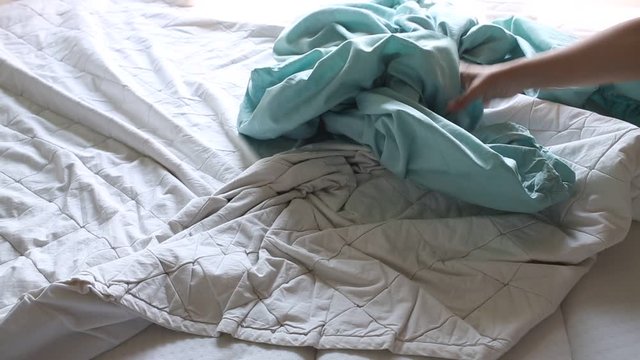 Woman's hand picking ivory pillow, turquoise crumpled bed sheet on white bed, Selective focus, Bedroom cleaning concept