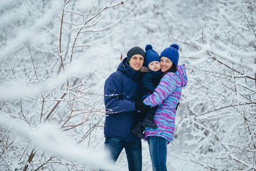 Fototapeta na wymiar Mom dad and little son embrace in a winter park. Young family for a walk in the forest