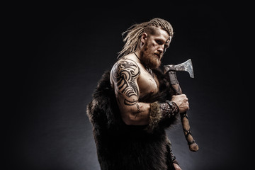 Medieval warrior berserk Viking with tattoo with axes attacks enemy. Concept historical photo - obrazy, fototapety, plakaty