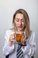 A blond woman in a white shirt and tie is drinking tea. There is a break in the train.