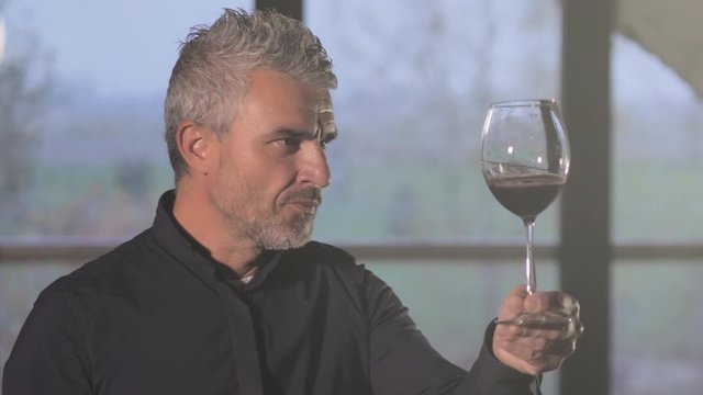 portrait of a handsome middle aged man smelling tasting a glass of red wine in the wine cellar