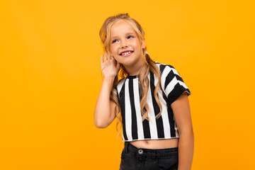 blond girl in a black and white striped t-shirt trying to hear something on a yellow background