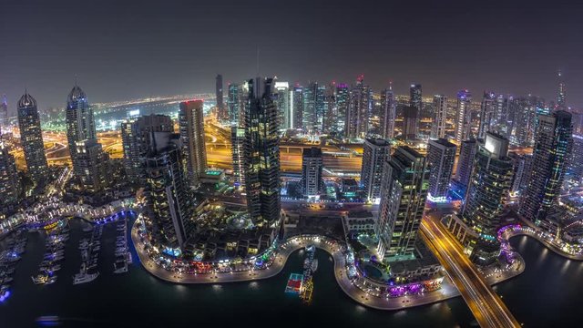 Aerial top view of Dubai Marina day to night transition timelapse. Promenade and canal with floating yachts and boats after sunset in Dubai, UAE. Illuminated modern towers and traffic on the road