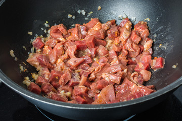 Marinated red veal tenderloin slices with onions are roasted in large cauldron for pilaf on stove.