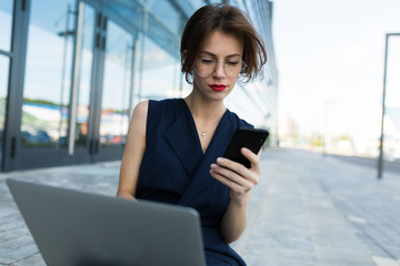Fototapeta premium Caucasian woman in office clothes do freelance with laptop and waits colleague near the office building