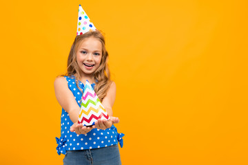 happy girl holds out a festive cap on an orange background with copy space