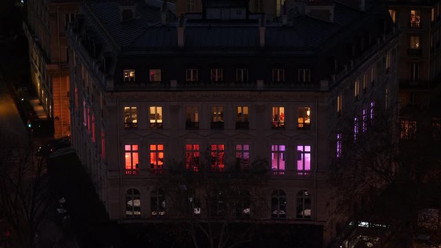 Windows with red and purple light in apartment building at night. Paris, France, aerial view. 