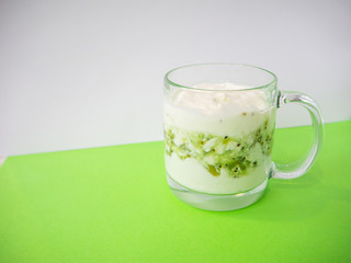Homemade yogurt with kiwi in a transparent cup on green background. Healthy breakfast and food, detox concept. Copy space, place for text