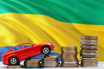 Gabon savings concept. Money for new automobile, toy car and coin piles standing on national flag...