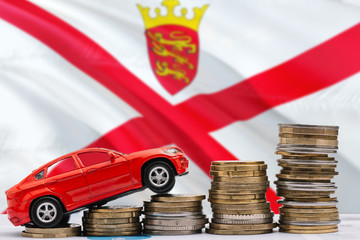 Fototapeta premium Jersey savings concept. Money for new automobile, toy car and coin piles standing on national flag background. Copy space for text.