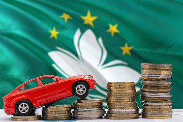 Macao savings concept. Money for new automobile, toy car and coin piles standing on national flag background. Copy space for text.