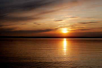 Golden, orange sunset on the sea sandy shore. The rays of sunset break through the clouds and beautifully glow in the water.