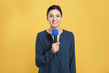 Young female journalist with microphone on yellow background