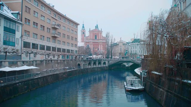 Snowing in Ljubljana city center on Presernov trg SLOWMOV 4K. Wide shot view of Ljubljana city center from over the bridge with river flowing bellow.
