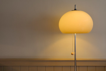 Vintage and retro 70's style floor lamp standing against a grey wall, with brown wooden paneling....
