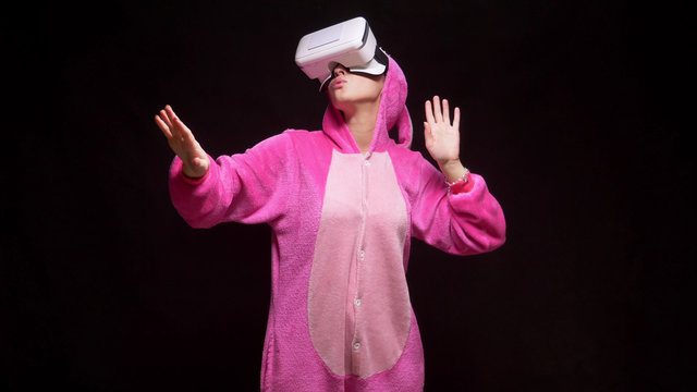 Fototapeta girl in pink pajamas kigurumi in VR glasses on a black background. pajama party