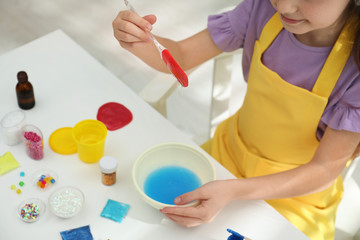 Little girl mixing ingredients with silicone spatula at table, closeup. DIY slime toy