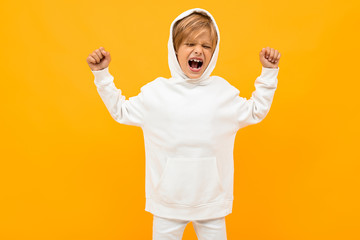 attractive blond boy in a white hoodie screaming out loud on an orange wall