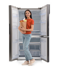 Fototapeta na wymiar Young woman with bag of groceries near empty refrigerator on white background