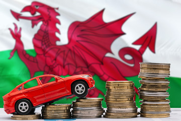 Wales savings concept. Money for new automobile, toy car and coin piles standing on national flag background. Copy space for text.