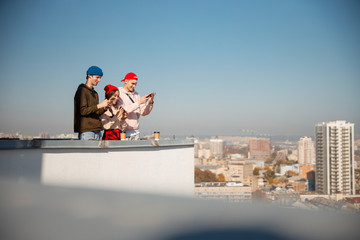 Three happy friends looking on their phones on roof