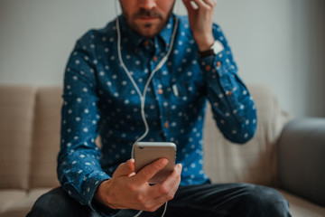 Front view of young man in blue shirt using smartphone with headphones connected