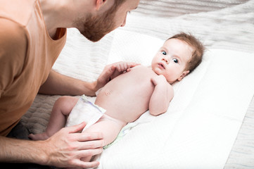 young modern father is caring for his newborn son. Changes the diaper on the bed. Hygiene and newborn care concept. Father's love and care. Father's day.