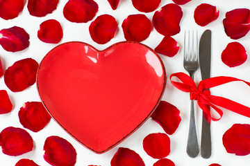 red heart-shaped plate, cutlery tied with a red ribbon and rose petals