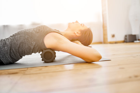 Young woman doing yoga lying on massager on rug in gym during day