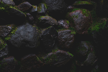 Dark wet stone texture background. Foggy faded black natural stones with green moss in cave. Close up