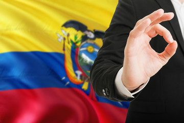 Ecuador acceptance concept. Elegant businessman is showing ok sign with hand on national flag background.