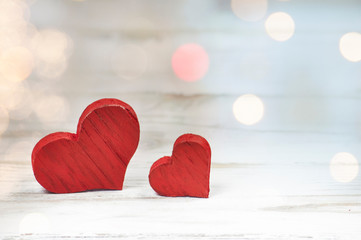 two red wooden hearts with texture small and large on white wooden background with bokeh effect in the background side view close up