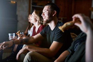 photo of man hanging out with friends eating pizza and watching tv at night