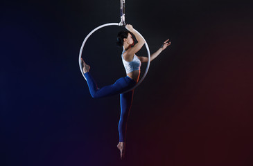 Young woman performing acrobatic element on aerial ring indoors © New Africa