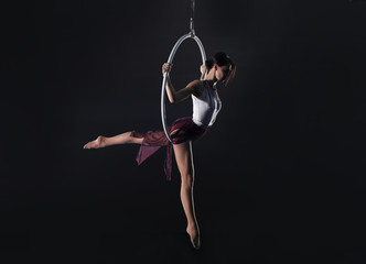 Young woman performing acrobatic element on aerial ring indoors © New Africa