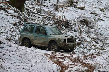 Off-road car rides down hill on snow and mud in forest