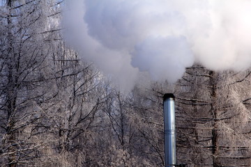 Beautiful winter day with white trees, blue sky and metal chimney with smoke