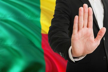 Benin rejection concept. Elegant businessman is showing stop sign with hand on national flag background.
