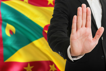 Grenada rejection concept. Elegant businessman is showing stop sign with hand on national flag background.