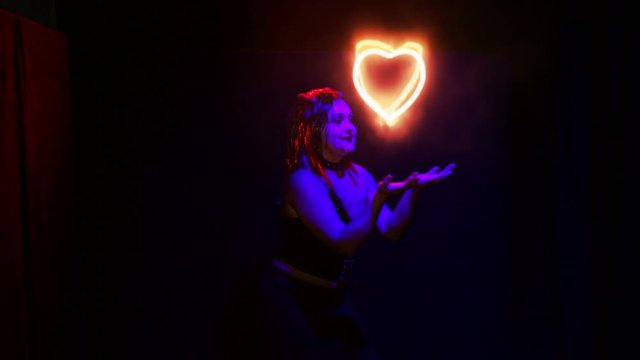 A woman in the image of a devil creates a sparkling heart in her hands