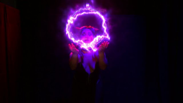 Woman the devil with an electric ball in her hands is dancing