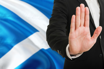 Scotland rejection concept. Elegant businessman is showing stop sign with hand on national flag background.
