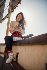Fototapeta na wymiar Happy young lady is typing while sitting on roof