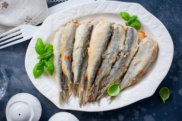 Whole grilled smelt fish on a white dish, selective focus, top view