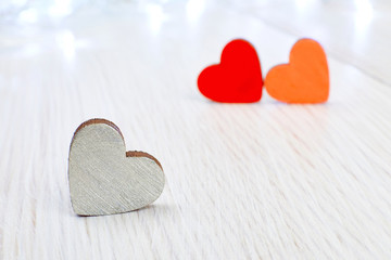 A gray wooden heart as opposed to two red on a light wooden background. The conception of unrequited love, unlucky Valentine's day