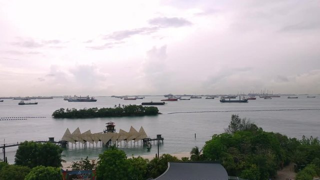 Aerial panning shot of the coast lines of sentosa showing the wings of time exhibit, the beach, coast and the container and transport ships in the distance