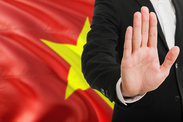 Vietnam rejection concept. Elegant businessman is showing stop sign with hand on national flag background.