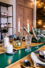 festive dinner. Fir branches with pine cones and vintage candlestick with burning white candles.Elegant Christmas or New Year Table setting with stylish glass,cutlery set and Christmas balls