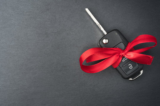 Car key with red bow on dark black slate plate background. Christmas or Valentine's Day gift or present abstract concept. Copy space on the left. Flat lay top view.