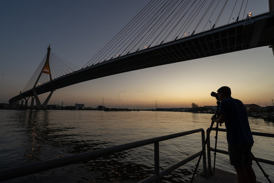 silhouette of photographer taking picture of bridge during sunset